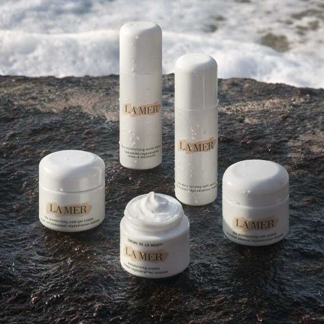 Group of moisturiser and lotion container and bottles sitting on a rock ledge near the ocean.